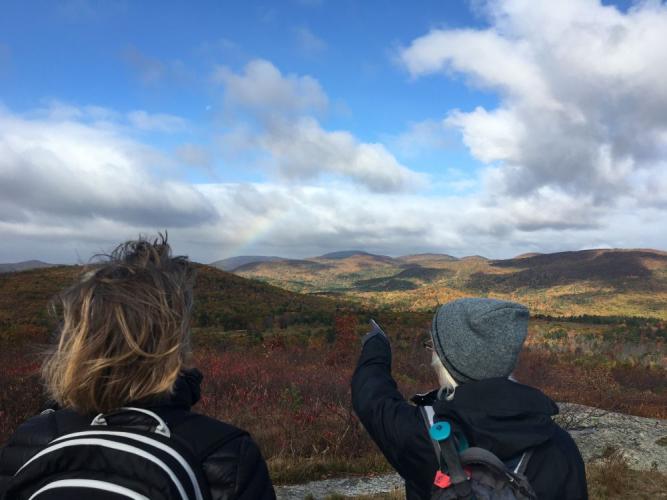 Hikers pointing to peaks of the eastern Belknap Range in Alton NH from the Forest Society Morse Preserve at the summit of Pine Mountain