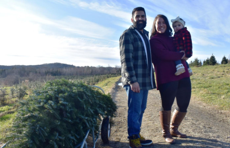 A couple poses with their infant and their fresh-cut Christmas tree at The Rocks.