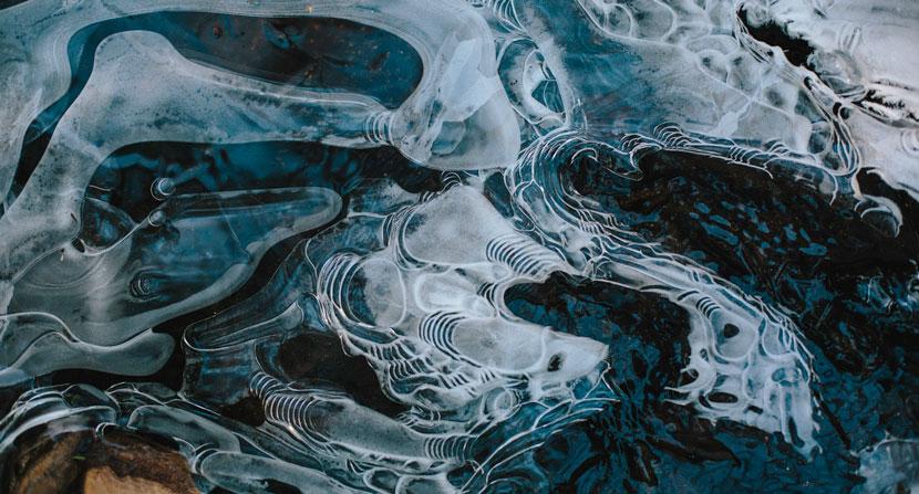 Flowing water forms ripples and bubbles as it freezes. Clear in some places, opaque in others.