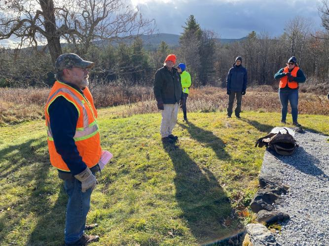 Staff in orange hats and vests view the new marker on a large granite stone at the forest.