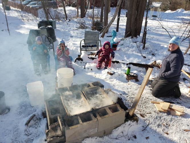 Gabe Roxby and his three daughters and wife sit outside around a fire while boiling sap.