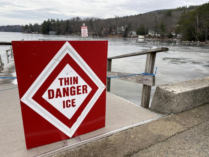 A red sign reading "Danger Thin Ice" is hung on a boat dock near a frozen lake