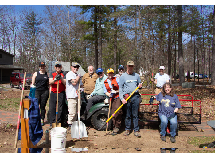 a group of people holding yard tools pose around a 4 wheeler 